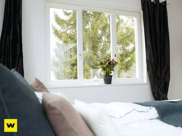 Helles Schlafzimmer mit großem Fenster, grünen Bäumen und Zimmerpflanze auf der Fensterbank.
