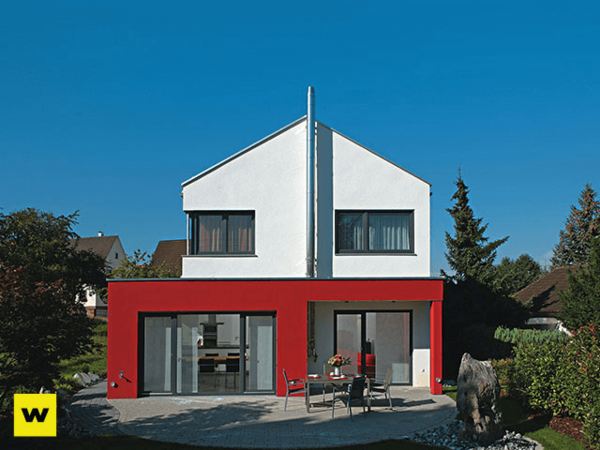 Modernes Einfamilienhaus mit roter Fassade und Garten bei klarem, blauem Himmel.