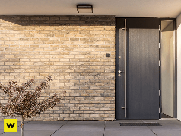 Moderne Haustür aus Aluminium vor heller Klinkerfassade mit kleinem Baum im Vordergrund.
